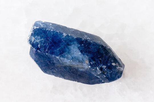 raw single blue sapphire crystal on white marble