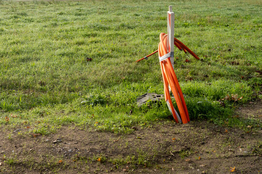 Bright orange utility conduit with wooden stake in grassy field