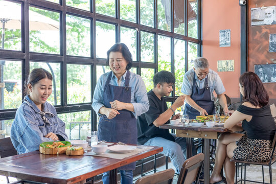 Restaurant small business senior couple owners taking food order from customers using digital tablet technology, teamwork service table, Asian husband and wife management professional support