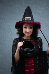 Funny witch holding magic wand and empty cauldron, worried about her potion. Perfect for Halloween, witches brew, and fairy tale villain. Vertical studio portrait with copy space.