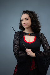 Charming mid-adult witch pointing a magic wand at copy space, looking at camera. Ideal for Halloween ads, trick or treat, magical spells, and fairy tale villain. Vertical studio portrait.