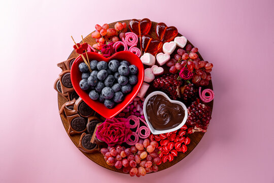 Snack board in shape of heart with berries, chocolate and sweets for Valentine's Day on a pink background top view