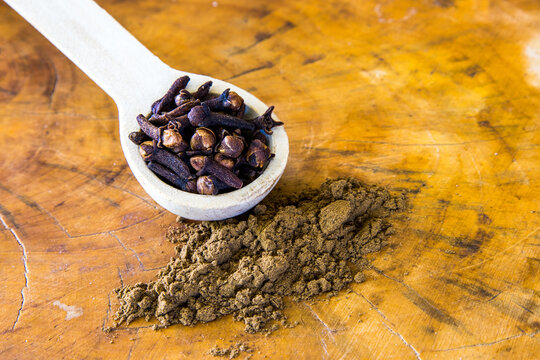 A wooden teaspoon filled with whole cloves and ground cloves.