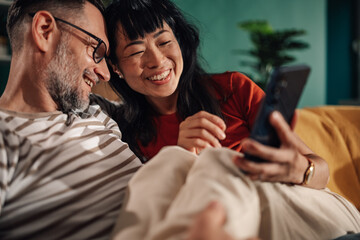 Happy couple relaxing on sofa browsing social media on mobile phone