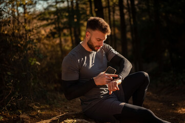 Male athlete using smartwatch and smartphone in forest