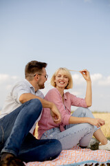 Fototapeta premium Couple enjoying a sunny day in a golden field while sitting on a blanket and sharing smiles