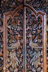 Intricate traditional Indonesian wood carving on a door, featuring birds and floral motifs. Balinese or Javanese cultural art and craftsmanship