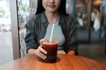 Woman holding a cup of iced Americano at a wooden table in a modern café setting.
