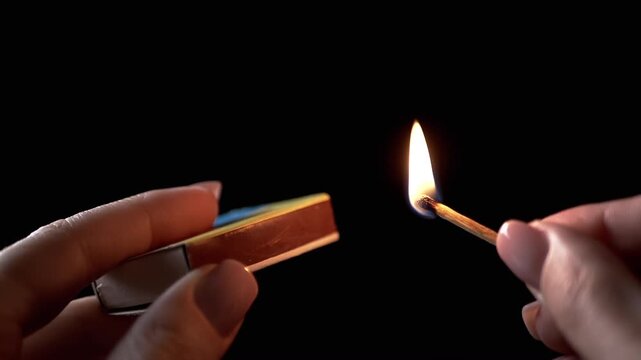 Burning match with matchbox in Dark Room. Female hands lighting match. Burning match with bright flame of fire. Room lighting. Power outage. Slow motion. Close-up.