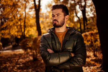 Young man in green jacket outdoors in peaceful autumn park with golden foliage and warm light portraying seasonal vibes