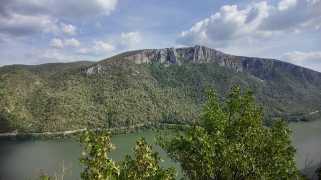 Danube river forming a deep gorge through the Carpathian mountains, creating the natural border between Serbia and Romania, with lush green forests covering the steep slopes under a blue sky