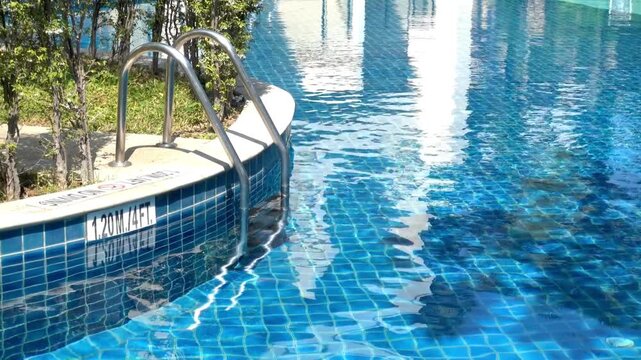 Swimming pool with blue tile and metal ladder on a sunny day