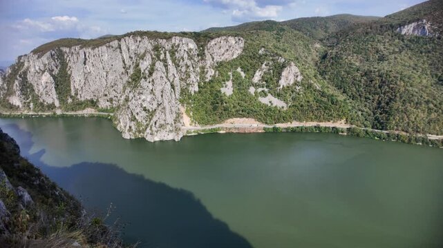 Danube river forming a deep gorge through the Carpathian mountains, creating the natural border between Serbia and Romania, with lush green forests covering the steep slopes under a blue sky