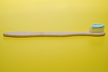 a bamboo toothbrush with toothpaste isolated on a yellow background