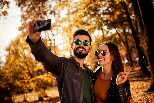 Happy couple taking a selfie in an autumn park surrounded by vibrant fall foliage during a sunny day outdoors - Powered by Adobe