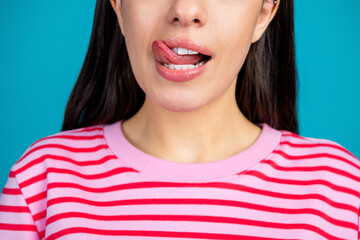 Close-up of a young fashionable woman in a pink striped shirt licking her lips against a bright blue background