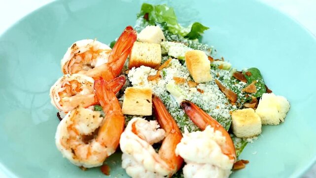 Delicious caesar salad with grilled shrimp, croutons, and parmesan cheese on blue plate