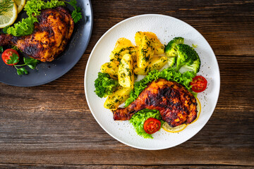 Oven roasted chicken leg with boiled potatoes and boiled broccoli on wooden table	