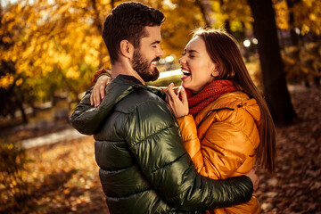 Romantic couple laughing together in an autumn park surrounded by vibrant foliage and warm sunlight embracing seasonal joy