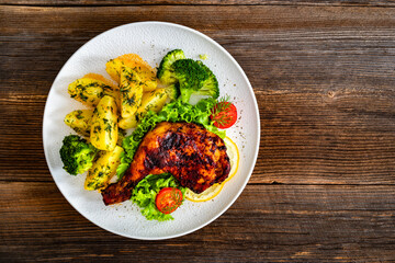 Oven roasted chicken leg with boiled potatoes and boiled broccoli on wooden table	