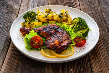Oven roasted chicken leg with boiled potatoes and boiled broccoli on wooden table	