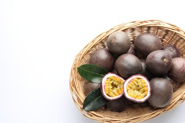 Fresh passion fruits with green leaves in wicker basket on white background, top view. Space for text