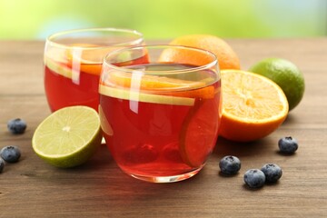 Tasty punch with fruits and blueberries on wooden table against blurred green background, closeup. Refreshing drink