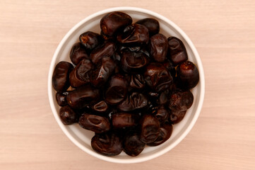 Sweet fresh brown dry dates on wooden background in white plate.