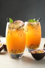 Tasty passion fruit drink with mint in glasses and fresh fruits on gray table, closeup