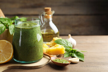 Fresh pesto sauce in jar and ingredients on wooden table, closeup. Space for text