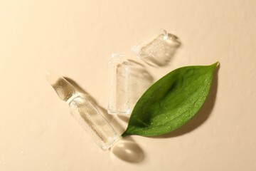 Glass ampoules with cosmetic product, leaf and water drops on beige background, flat lay