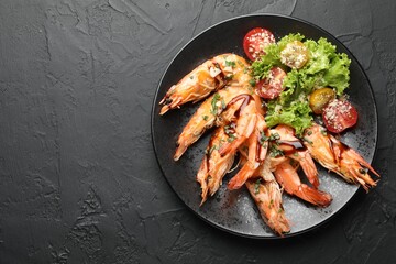 Delicious seafood dish. Tasty grilled shrimps served with salad on black table, top view. Space for text