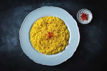 Risotto alla Milanese in a white aristocratic dish on the dark table. A classic Lombard saffron risotto recipe. Cuisine the North Italy