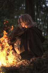 Mysterious woman warms hands by campfire in enchanting forest, evoking fantasy and adventure for...