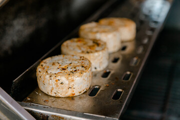 Grilled cheese patties with herbs and spices cooking on a metal tray, rustic and appetizing food concept