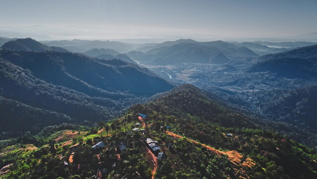Breathtaking aerial view capturing a vast mountainous landscape adorned with lush forests and a small village nestled in the greenery of Chiang Mai Province, Thailand