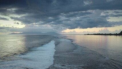 Aerial view of ocean waves breaking on the shore of Tahiti island at sunset, with dramatic clouds...