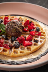 Waffle dessert with chocolate ice cream and fresh berries on pink plate