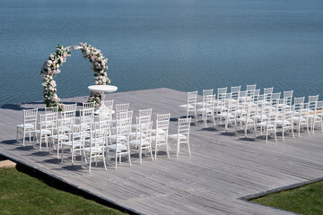 Wooden pontoon decorated with a floral arch, prepared for a romantic outdoor religious wedding ceremony by the water