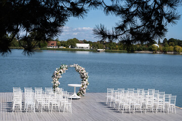 Wooden pontoon decorated with a floral arch, prepared for a romantic outdoor religious wedding ceremony by the water