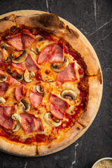 Pizza with ham and mushrooms on black stone table background