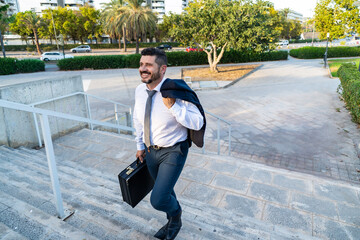 Confident businessman walking up stairs with briefcase outdoors