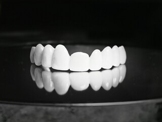 Fototapeta premium A row of white ceramic dental teeths on a reflective surface, creating a mirror image below.