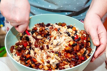 A close-up shot of someone mixing fruits and nuts into a batter in a bowl.