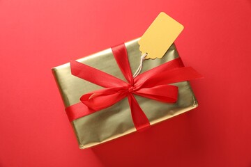 Gift box with blank tag on red background, top view