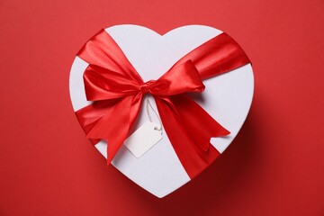 Heart-shaped gift box with blank tag on red background, top view