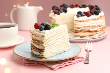 Piece of tasty crepe cake with berries served on pink wooden table against blurred lights, closeup