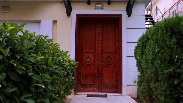 Elegant brown solid wood door of a classic-style house, sheltered by a transparent glass canopy, amidst vibrant green foliage, capturing timeless architecture . Travel to Athens, Greece.