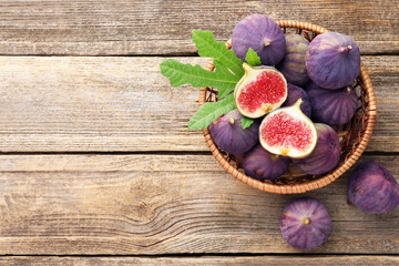 Fresh ripe figs and green leaf in wicker basket on wooden table, flat lay. Space for text