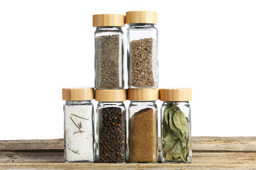 Many different aromatic spices in glass jars on wooden table against white background